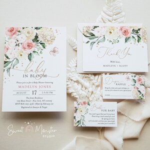 May include: A set of baby shower invitations featuring a floral design. The invitation has a pink and white floral pattern with gold accents. The text on the invitation reads "Baby in Bloom" and includes the date, time, and location of the shower. The thank you card features the same floral design and the text "Thank You" with the names "Madelyn & Scott".