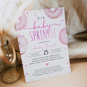 Może przedstawiać: Różowe i białe zaproszenie na baby shower z motywem pączków. Zaproszenie zawiera napis "It's a baby sprinkle" oraz datę, godzinę i miejsce wydarzenia. Zawiera również imię osoby, której to wydarzenie jest poświęcone, Ainsley Stewart.