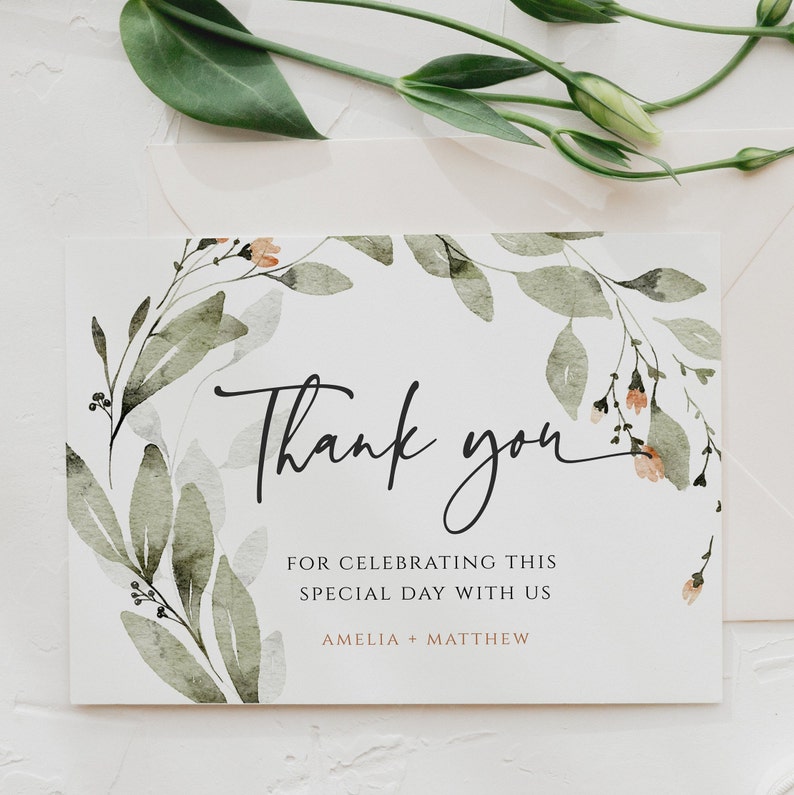 May include: Thank you card with a watercolor floral design in shades of green and peach. The card says "Thank you" in black script and "For celebrating this special day with us Amelia + Matthew" in black text.