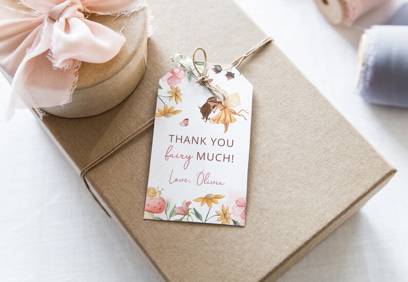 Pode incluir: Uma etiqueta de presente branca com uma ilustra&ccedil;&atilde;o em aquarela de uma fada com flores e borboletas. O texto na etiqueta diz "Obrigado fada muito! Com amor, Olivia."