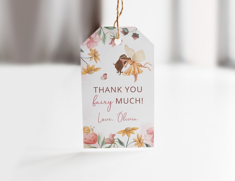 Pode incluir: Uma etiqueta de agradecimento com uma ilustra&ccedil;&atilde;o em aquarela de uma fada com cabelo castanho e um vestido amarelo voando sobre um campo de flores. O texto na etiqueta diz "Obrigado fada! Com amor, Olivia."