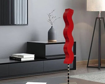 Op de afbeelding: Een rood abstract beeldhouwwerk met een golvend ontwerp staat op een zwarte basis. Het beeldhouwwerk staat op een zwarte salontafel in een moderne woonkamer.
