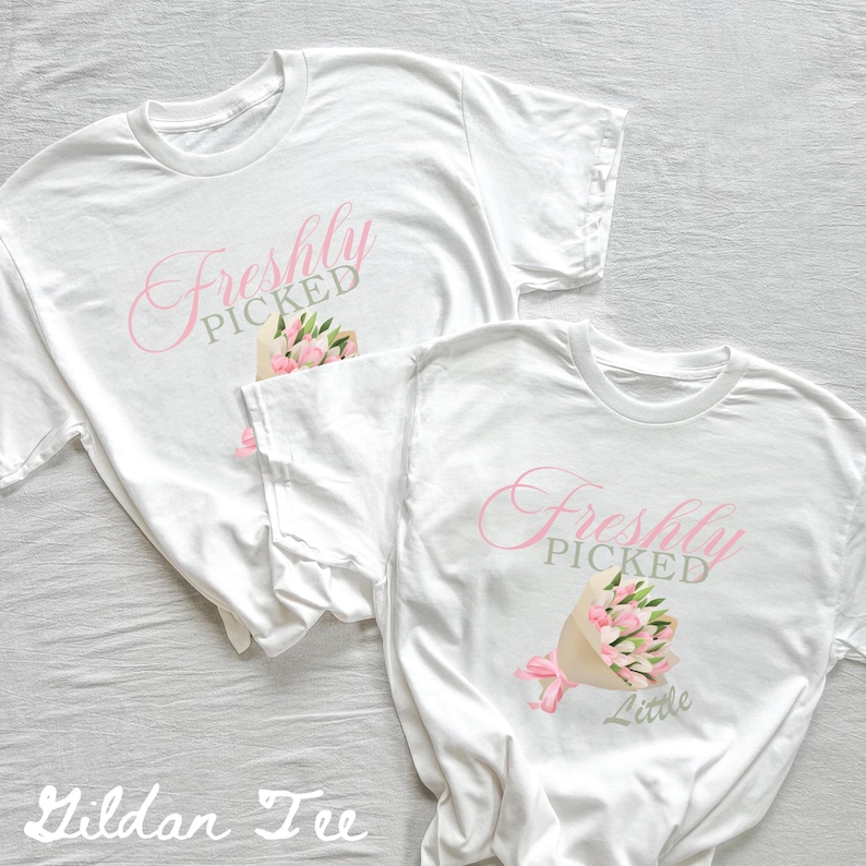May include: Two white t-shirts with the text "Freshly Picked" in pink and gray. One shirt has the text "Little" below the main text. Both shirts feature a bouquet of pink flowers.