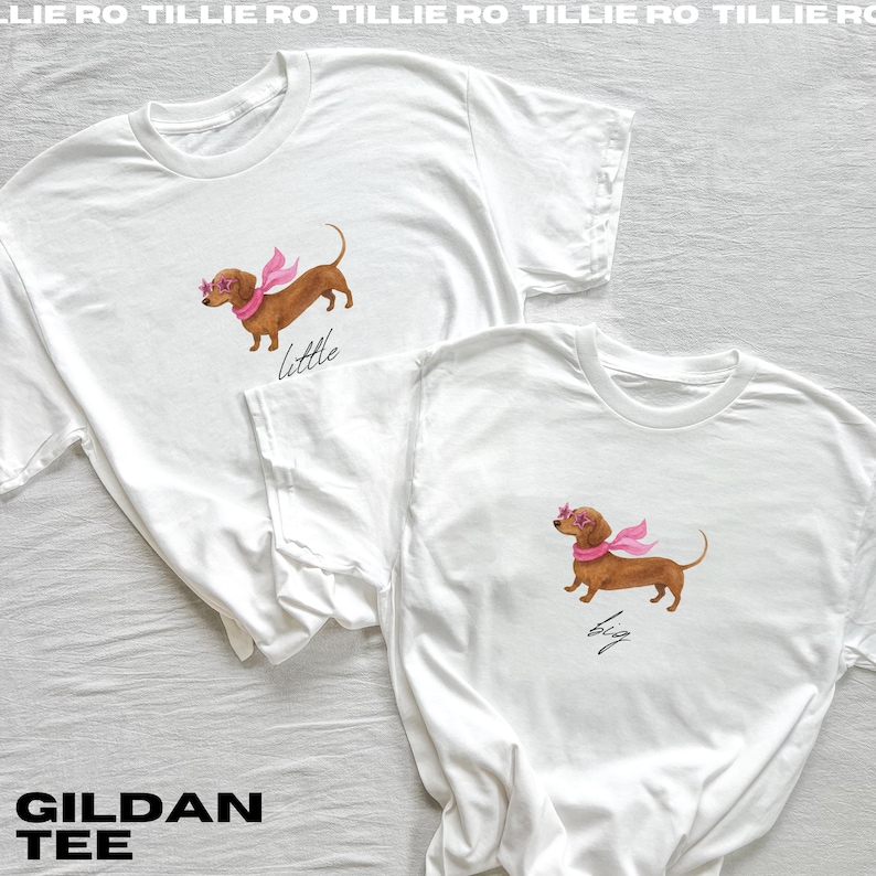 May include: Two white Gildan tee shirts. One shirt has a watercolour illustration of a brown dachshund wearing pink sunglasses and a pink scarf with the word "little" below. The other shirt has the same illustration with the word "big".