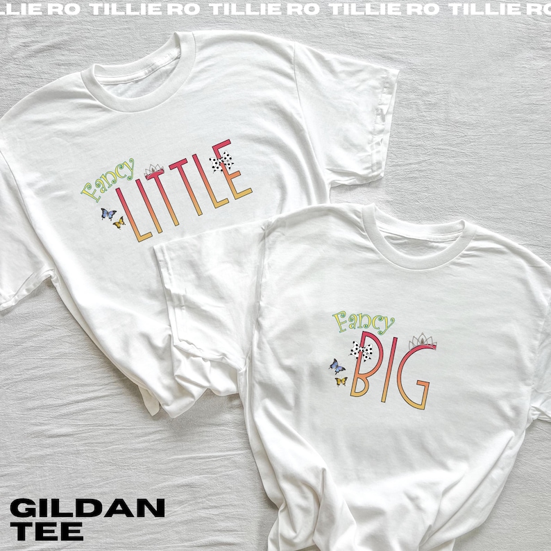 Pode incluir: Duas camisetas Gildan brancas com as palavras "Fancy Little" e "Fancy Big" em letras coloridas e estilizadas. Borboletas e detalhes florais decoram o texto. As camisetas s&atilde;o roupas casuais.