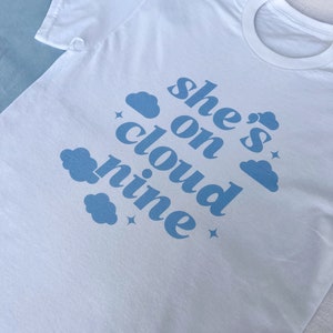 May include: White t-shirt with blue text that reads "she's on cloud nine" with blue cloud illustrations.