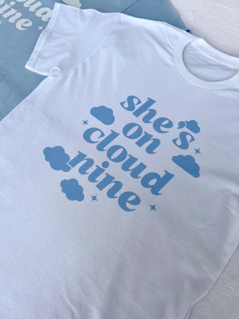 May include: White t-shirt with blue text that reads "she's on cloud nine" with blue cloud illustrations.