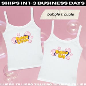 May include: Two white tank tops with spaghetti straps. One top has the text "Hubba Little" and the other says "Hubba Big", both in yellow and blue bubble-themed designs. The phrase "bubble trouble" is also visible.