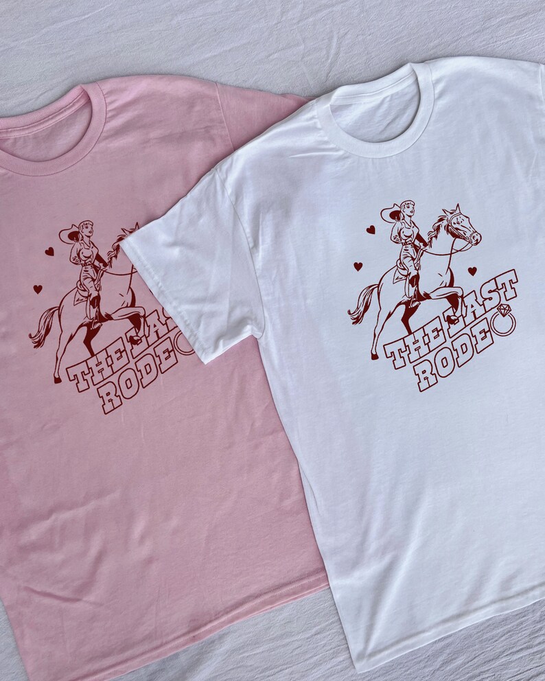 May include: Two t-shirts with a graphic of a woman riding a horse. The text on the shirts reads "The Last Rodeo". One shirt is pink and the other is white.