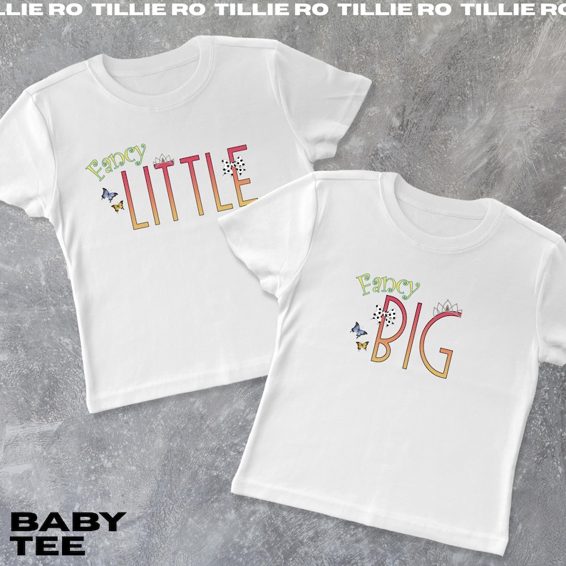 Pode incluir: Duas camisetas brancas para beb&ecirc;s com as palavras "Fancy Little" e "Fancy Big" em letras coloridas. As camisas t&ecirc;m gr&aacute;ficos de borboletas e coroas. O texto "BABY TEE" est&aacute; na parte inferior.