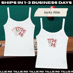 May include: Two white tank tops with spaghetti straps. Each top features a playing card design with red hearts. One top has the word "TILLIE" on the cards, and the other has the word "BIG". The text "lucky little" is above the tops.
