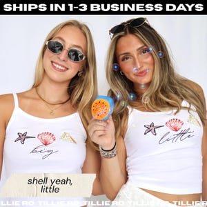May include: Two women wearing white tank tops with seashell graphics and the words "big" and "little". One woman holds a blue bubble machine. The text "shell yeah, little" is also visible. Sunglasses are worn by one woman.
