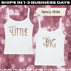 Pode incluir: Duas camisetas brancas com as palavras "Fancy Little" e "Fancy Big" em letras coloridas. A parte superior "Little" tem borboletas e a parte superior "Big" tem um gr&aacute;fico de coroa. O fundo &eacute; um padr&atilde;o de lantejoulas rosa.