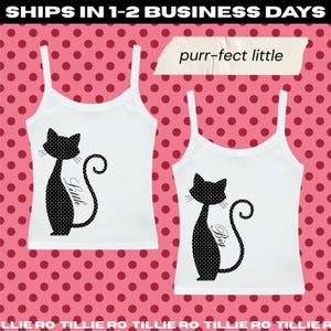 May include: Two white tank tops featuring a black cat graphic with white polka dots. One cat has the word Little printed on its body, and the other has the word Big. A piece of tape above the shirts displays the text purr-fect little.