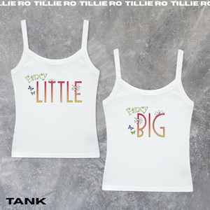 Pode incluir: Duas camisetas brancas com as palavras "Fancy LITTLE" e "Fancy BIG" em letras coloridas. As camisetas t&ecirc;m al&ccedil;as finas e s&atilde;o decoradas com borboletas e desenhos florais. A palavra "TANK" est&aacute; na parte inferior.