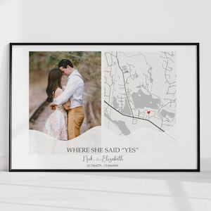 Puede incluir: Impresión enmarcada en negro con una foto de una pareja y un mapa. El mapa resalta una ubicación con un marcador rojo. El texto dice "WHERE SHE SAID 'YES'" con nombres y coordenadas. El fondo es blanco.