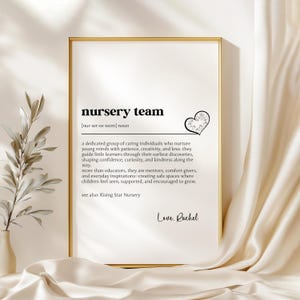 May include: A framed print with the words "nursery team" in black text. The definition of nursery team is provided below the title. A decorative heart is on the right side of the text. The print is signed "Love, Rachel".