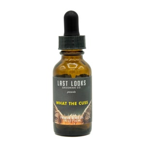 May include: A brown glass bottle with a black dropper top and a black label that reads "LAST LOOKS GROOMING CO. presents WHAT THE CUSS PREMIUM BEARD OIL 1 FL OZ 30 ML".