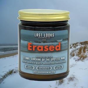 Könnte beinhalten: Ein braunes Glasgefäß mit einem goldenen Deckel und einem Etikett mit der Aufschrift "Last Looks Grooming Co. präsentiert Erased" inspiriert vom Film "Eternal Sunshine of the Spotless Mind". Das Etikett enthält auch den Text "Snowy Montauk Beach Bookstore Frozen River" und "Handcrafted in Hollywood, CA".
