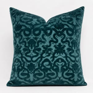 May include: A square throw pillow in a deep teal color featuring a raised velvet texture. The surface displays a repeating damask-inspired pattern with intricate swirling lines and floral motifs that create a tactile, monochromatic design.