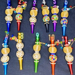 May include: Eleven colorful glass smoking pipes with gold accents and crystal embellishments. Each pipe has a different color and design. The pipes are numbered 1 through 11.