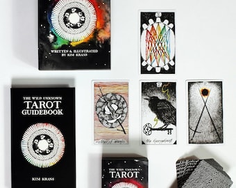 May include: A tarot deck and guidebook set. The black box and guidebook feature the text "THE WILD UNKNOWN TAROT" with a colorful circular design. Several tarot cards are displayed, including "mother of wands" and "the hierophant".
