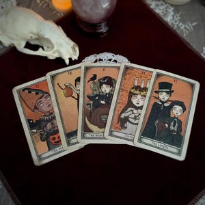 May include: Five tarot cards with illustrations of figures in a vintage style. The cards feature characters with pale skin and dark eyes, set against an orange background. The cards are labeled with titles such as "The Fool" and "The Lovers".
