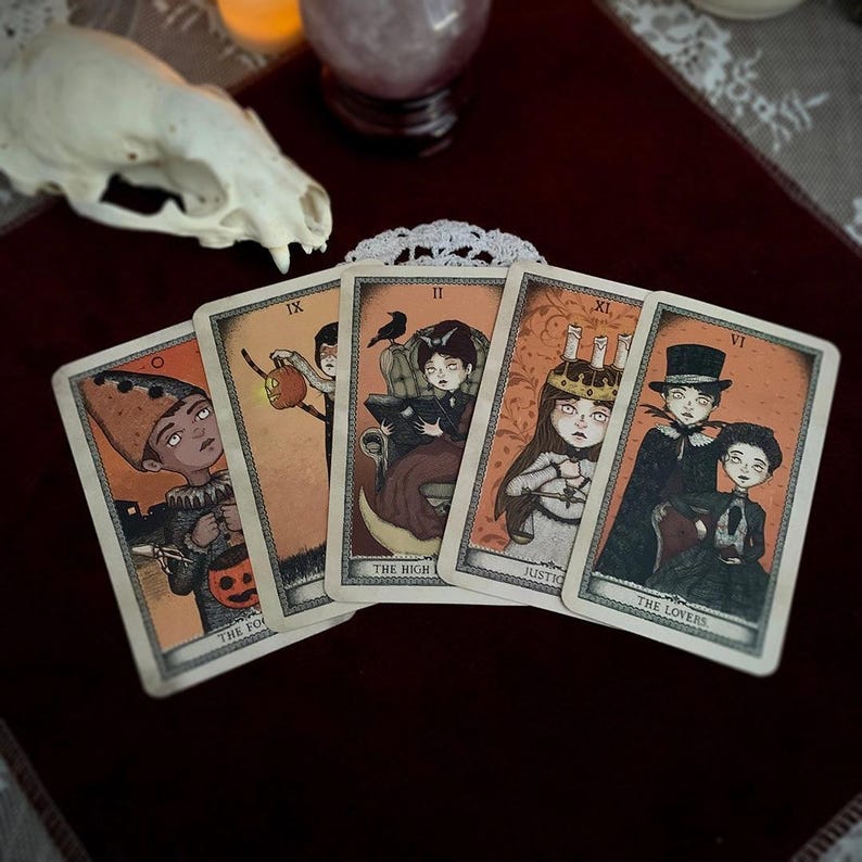 May include: Five tarot cards with illustrations of figures in a vintage style. The cards feature characters with pale skin and dark eyes, set against an orange background. The cards are labeled with titles such as "The Fool" and "The Lovers".