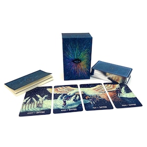 Op de afbeelding: Een tarotkaartspel met een donkerblauwe doos met een kleurrijk oogontwerp. De set bevat een boekje en verschillende kaarten met illustraties en tekst, waaronder "Eight of Swords", "Nine of Swords", "Ten of Swords" en "Page of Swords".