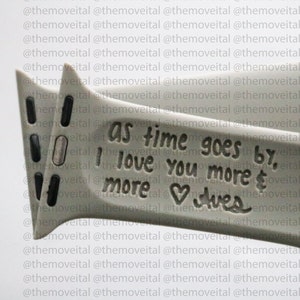 以下が含まれることがあります： ハートと「As time goes by, I love you more & more」という刻印が施されたグレーの金属製のブレスレットです。