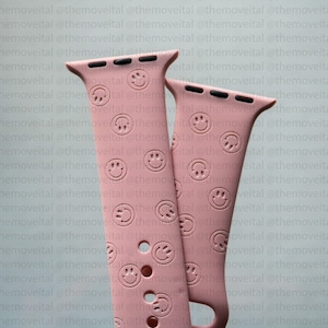 May include: Two pink Apple Watch bands with a repeating pattern of smiley faces and paw prints.
