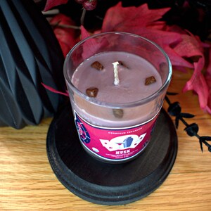 May include: A glass jar candle with a pink wax and brown decorative pieces. The label reads "Delicious Treasures" and "Musk" with a red and white design.