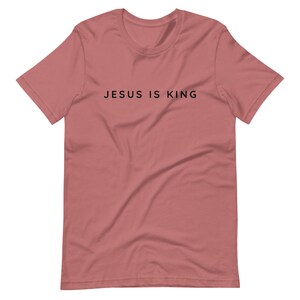 May include: A dusty rose short-sleeved t-shirt with the text "JESUS IS KING" printed in black on the front.