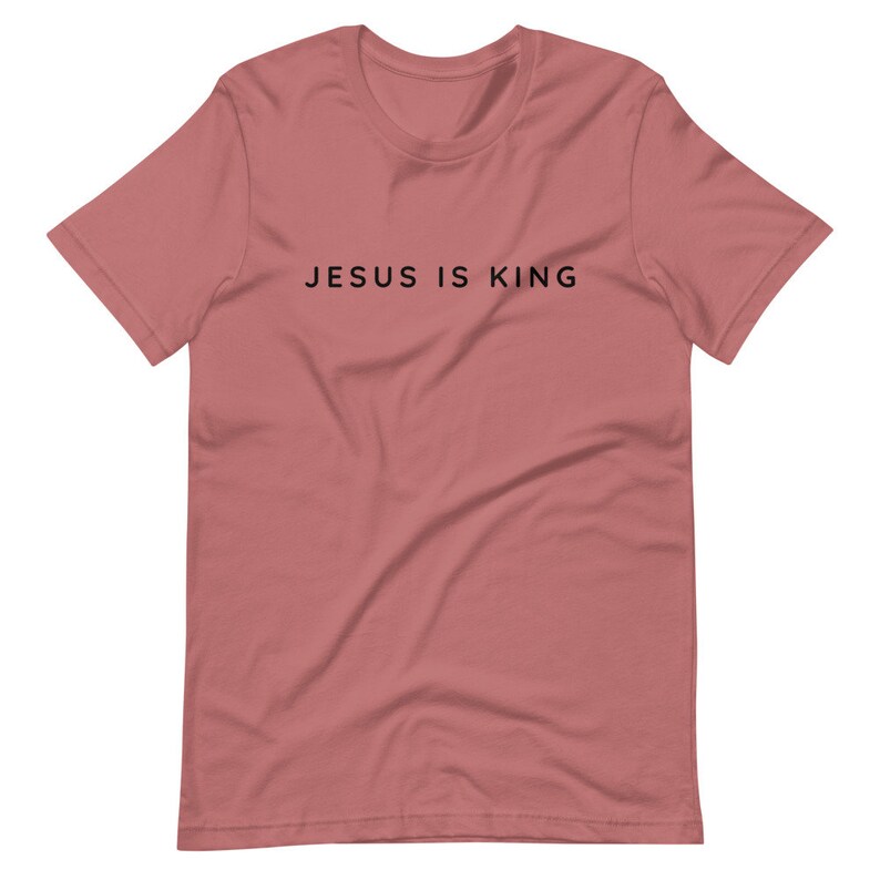 May include: A dusty rose short-sleeved t-shirt with the text "JESUS IS KING" printed in black on the front.