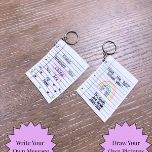 Puede incluir: Dos llaveros hechos a mano con dise&ntilde;os de papel rayado. Uno dice "Always Remember How Loved You Are!" con corazones. El otro dice "Have the BEST School year!" con un arco&iacute;ris. Ambos tienen llaveros de metal.