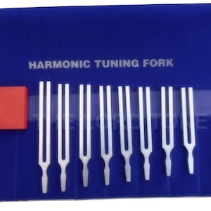 Op de afbeelding: Een set van acht zilveren stemvorken in een blauwe fluwelen koffer met de woorden "HARMONIC TUNING FORK" gedrukt op de koffer.