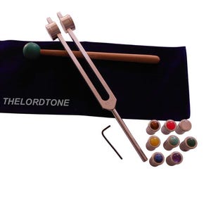 May include: A silver tuning fork with a wooden mallet and a dark blue velvet pouch. The pouch has the text "THELORDTONE" printed on it. Also included are several small, colorful gemstone applicators and a small black wrench.