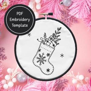 May include: A black and white embroidery hoop with a Christmas stocking design. The stocking is filled with gifts and greenery. The text "PDF Embroidery Template" is in a black circle.