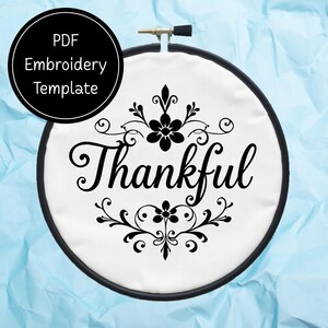 Peut inclure: Un cercle à broder avec un tissu blanc, orné du mot "Thankful" en écriture noire et de motifs floraux. Un cercle noir avec "PDF Embroidery Template" est en haut à gauche. Le tout sur fond bleu clair.