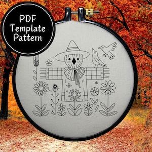 Peut inclure: Un cercle à broder noir avec un tissu crème orné d'un dessin au trait noir d'un épouvantail, de fleurs et d'oiseaux. Le texte "PDF Template Pattern" est dans un cercle noir en haut à gauche.