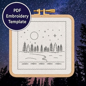 Può includere: Un telaio da ricamo quadrato in legno contenente tessuto bianco con un disegno a linee nere di un paesaggio notturno con luna piena, stelle, una foresta di pini, un sentiero tortuoso ed erba, con un badge che riporta PDF Embroidery Template.