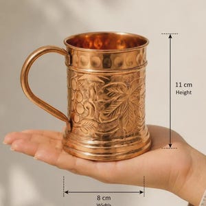 May include: A copper mug featuring an embossed grape and leaf pattern on the exterior, a smooth handle, and a textured rim. The mug measures 11 cm in height and 8 cm in width, as indicated by the measurement labels printed on the image.