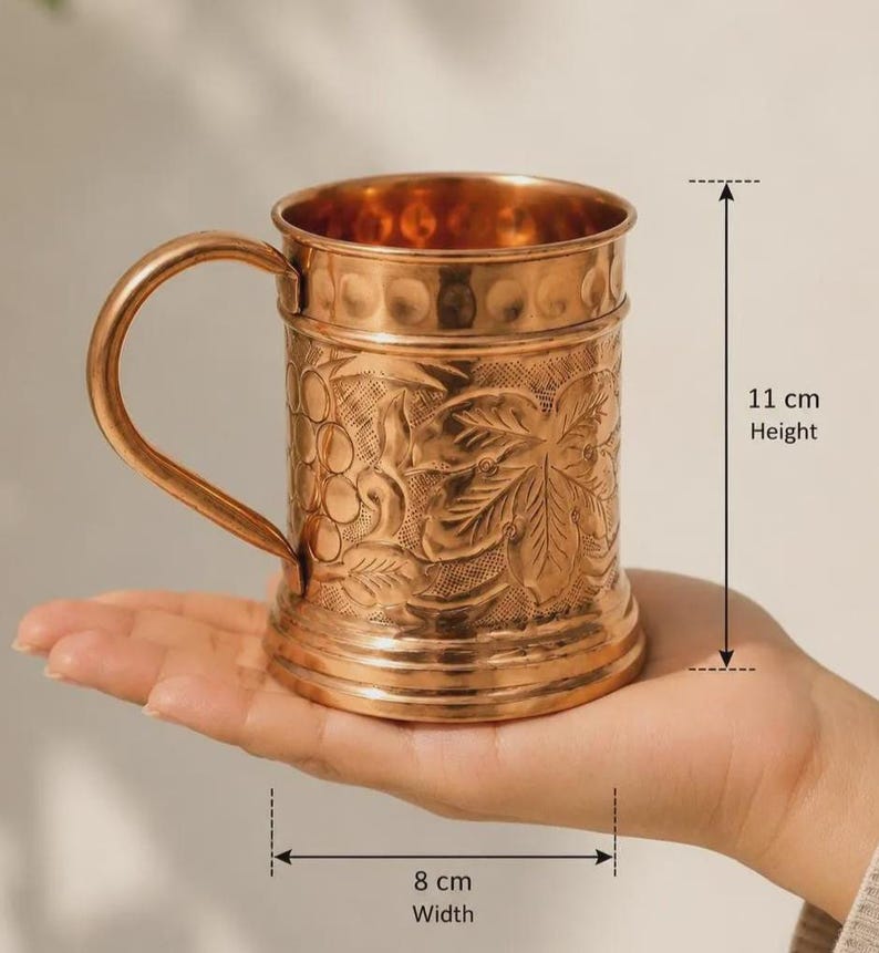 May include: A copper mug featuring an embossed grape and leaf pattern on the exterior, a smooth handle, and a textured rim. The mug measures 11 cm in height and 8 cm in width, as indicated by the measurement labels printed on the image.