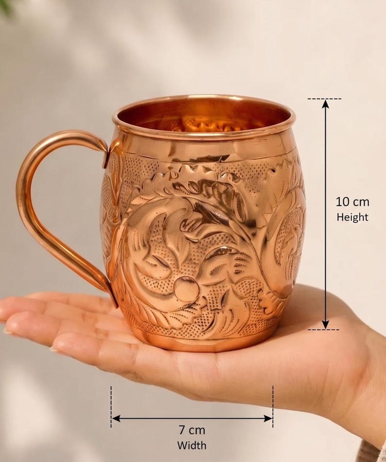 May include: A copper mug with an embossed floral pattern and a curved handle. The mug features a height of 10 cm and a width of 7 cm as indicated by the measurement markers. The exterior surface has a polished metallic finish with intricate detailing.