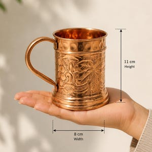 May include: A copper mug with a curved handle and embossed grape and leaf patterns on the exterior. The mug features a smooth rim and base, with a height of 11 cm and a width of 8 cm as indicated by the measurement markers on the image.