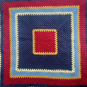 May include: A crocheted square blanket with a navy blue center and a multi-colored border. The border is made up of red, yellow, light blue, and white stripes.
