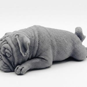 A detailed handmade vegan soap gift, sculpted in the shape of a pug dog lying flat on its stomach in a sleeping position, showing realistic skin folds and fur texture
