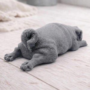 A detailed handmade vegan soap gift, sculpted in the shape of a pug dog lying flat on its stomach in a sleeping position, showing realistic skin folds and fur texture