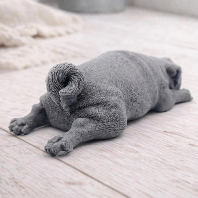 A detailed handmade vegan soap gift, sculpted in the shape of a pug dog lying flat on its stomach in a sleeping position, showing realistic skin folds and fur texture