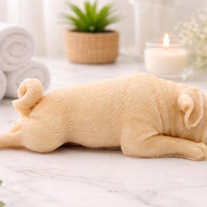 handmade vegan soap in the shape of a realistic sleeping pug dog lying flat, showing detailed wrinkles and fur texture, displayed in a spa-like setting with a candle and lavender.